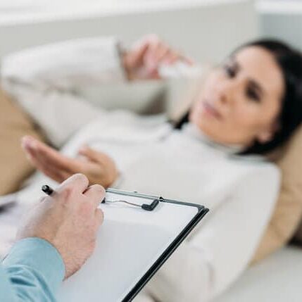 cropped shot of psychotherapist writing on clipboard and young patient in depression lying on couch